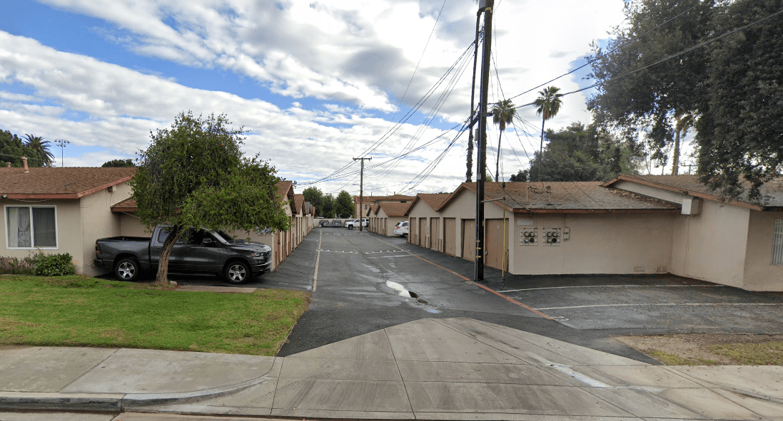A residential street with houses on both sides and cars parked on the side.